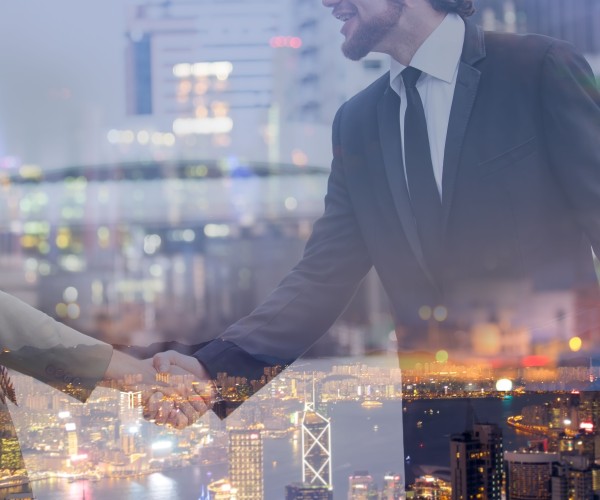 In the backdrop, a businessman shakes hands with a metropolitan view.